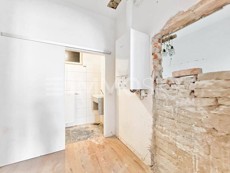 Raum in Sanierung mit Zugang zu einem kleinen Badezimmer und sichtbarem Boiler.
