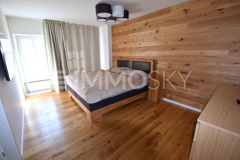 Helles Schlafzimmer mit Holzbett, Holzakzentwand, Holzboden und Zugang zu einem Balkon oder einer Terrasse.
