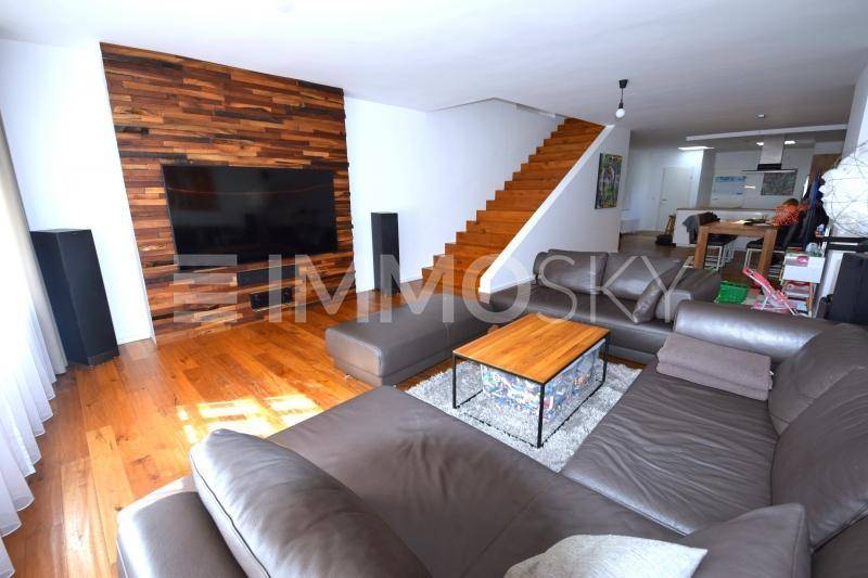 Geräumiges Wohnzimmer mit Ledersofa, Holzboden und einer markanten Holzwand, die den Fernseher umrahmt.