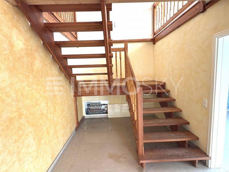 Holztreppe in einem Flur mit strukturierten Wänden und einem Sicherungskasten darunter.