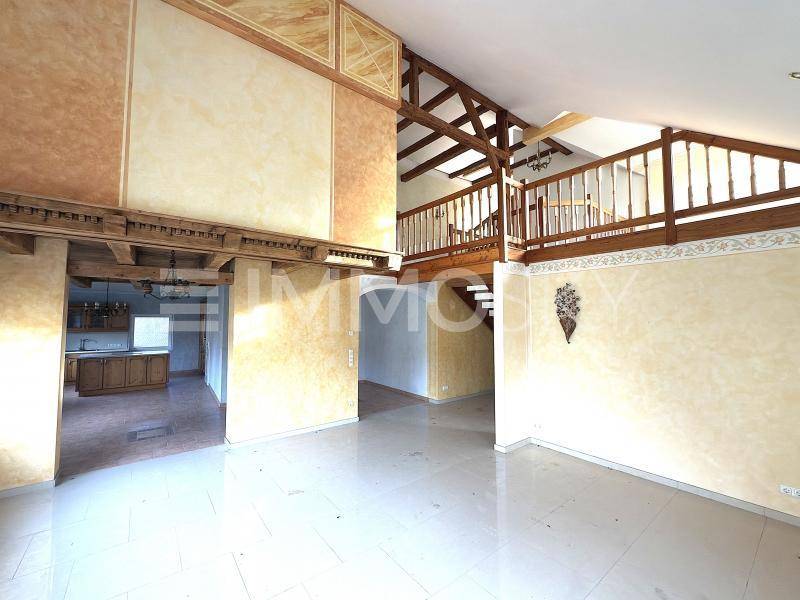 Geräumiger Wohnbereich mit hohen Decken, sichtbaren Holzbalken und einer Holztreppe zur Galerie.