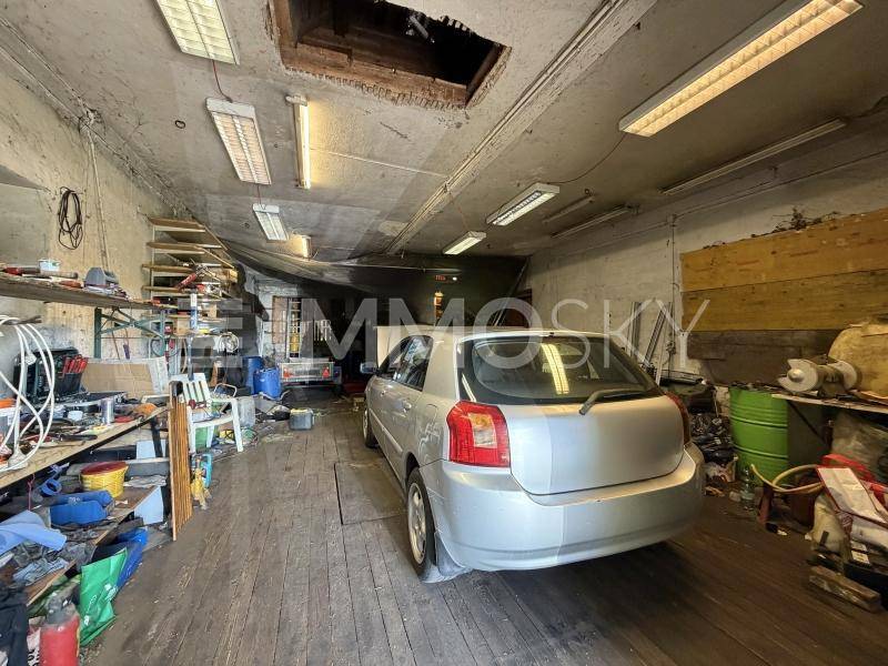 Geräumige Garage mit einem geparkten Auto, Werkstattregalen und sichtbaren Deckenleuchten.