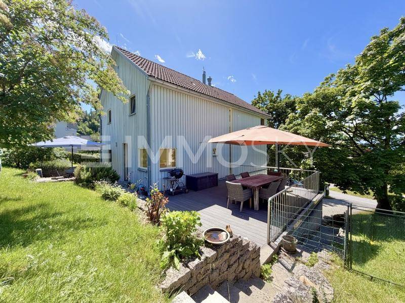 Große Holzterrasse mit Esstisch und Sonnenschirm, umgeben von einem grünen Garten.