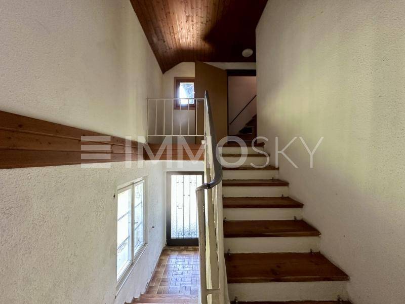 Holztreppe mit Geländer und Fenstern, die verschiedene Ebenen des Hauses verbindet.