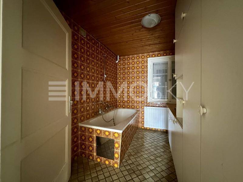 Badezimmer im Stil der 80er Jahre mit Badewanne, gemusterten Fliesen und Holzdecke.