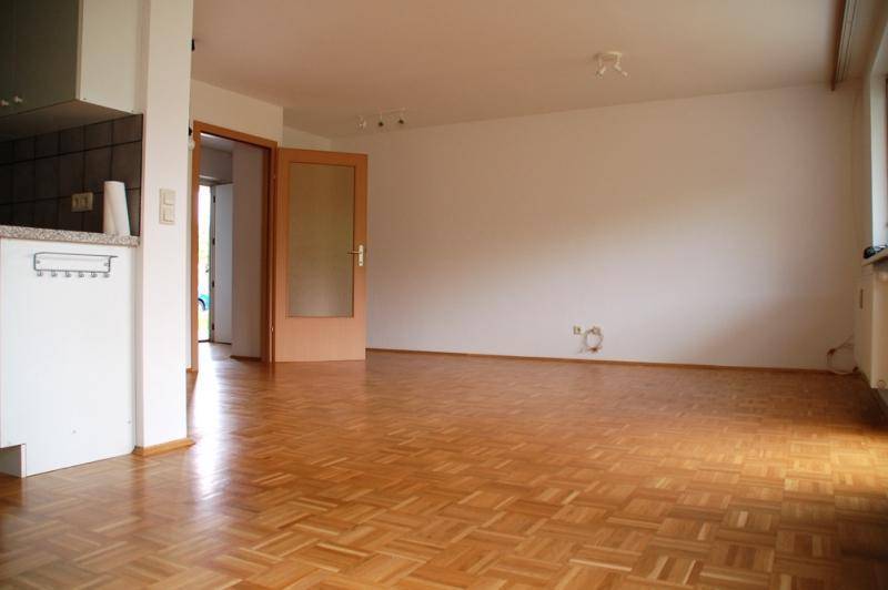 Heller Wohnbereich mit Parkettboden und teilweisem Blick auf die angrenzende Küche.
