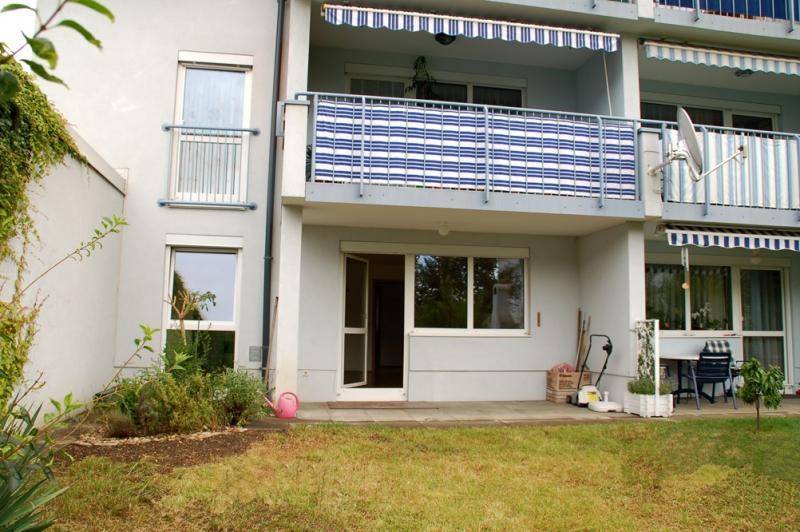 Erdgeschoss-Terrasse mit Rasenfläche und darüberliegendem Balkon mit Markise.
