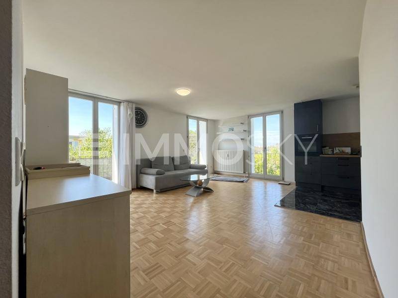 Geräumiger Wohnbereich mit Parkettboden, Sofa und großen Fenstern mit Zugang zum Balkon.