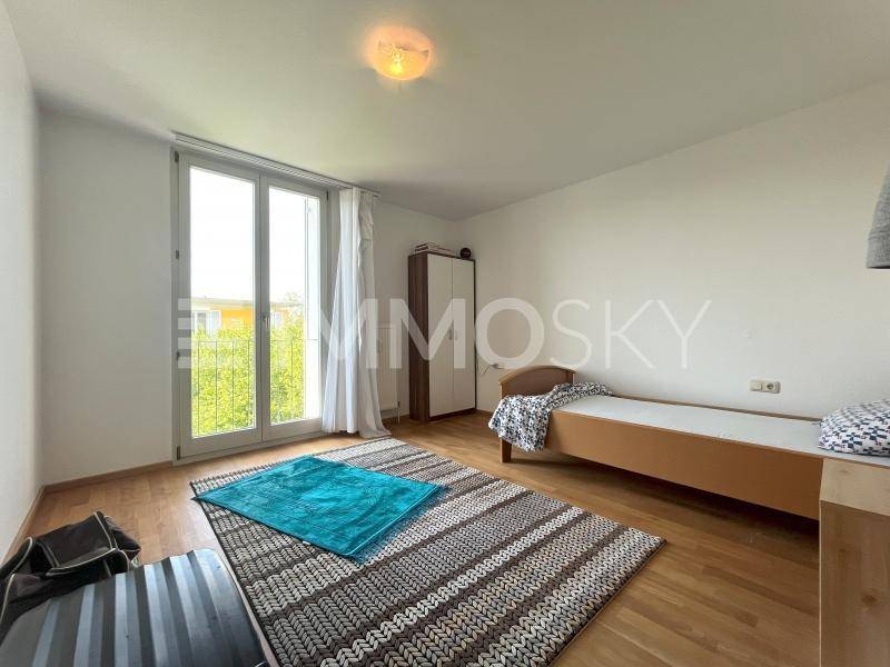 Helles Schlafzimmer mit Parkettboden, Einzelbett und großem Fenster mit französischem Balkon.