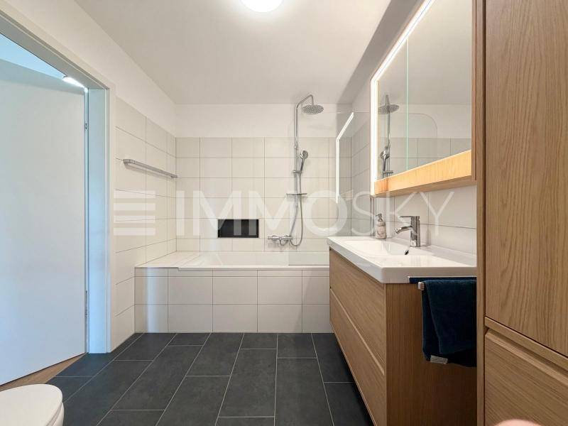 Modernes Badezimmer mit Badewanne, integrierter Dusche und stilvollen dunklen Bodenfliesen.