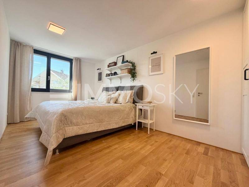 Helles Schlafzimmer mit Holzboden, großem Bett und einem Fenster mit Blick nach draußen.