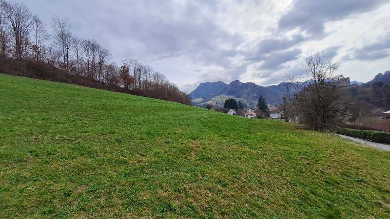Ausgedehnte grüne Grasfläche mit Fernblick auf eine Siedlung und die beeindruckende Bergkulisse unter einem bewölkten Himmel.