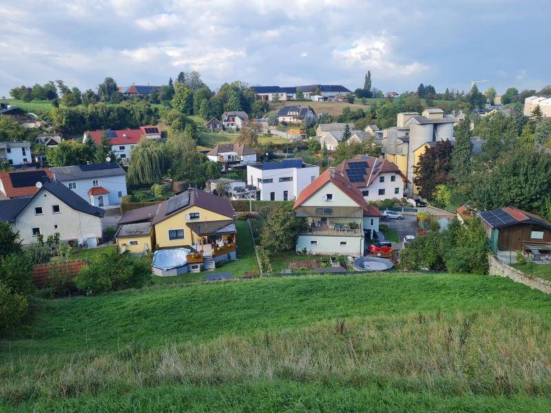 Panoramablick auf eine ländliche Wohnsiedlung mit verschiedenen Häusern und grünen Feldern im Vordergrund.
