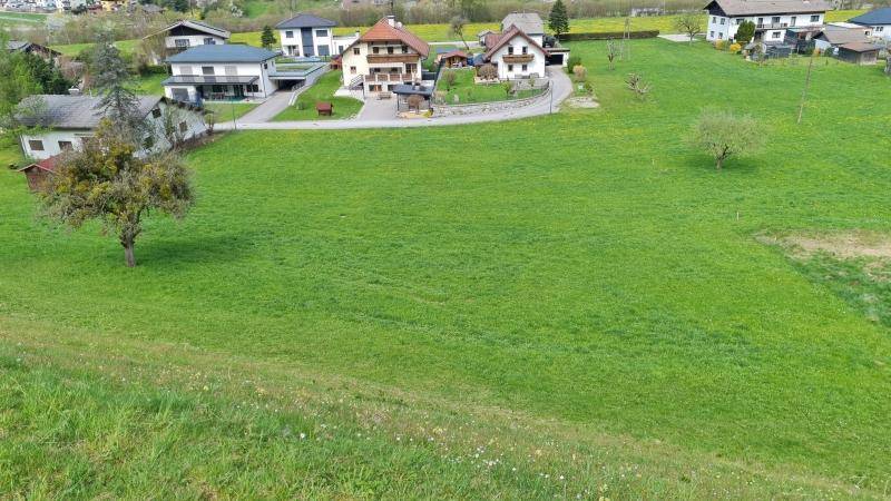 Aussicht auf eine weitläufige grüne Fläche mit Siedlungshäusern und sanften Hügeln am Horizont.