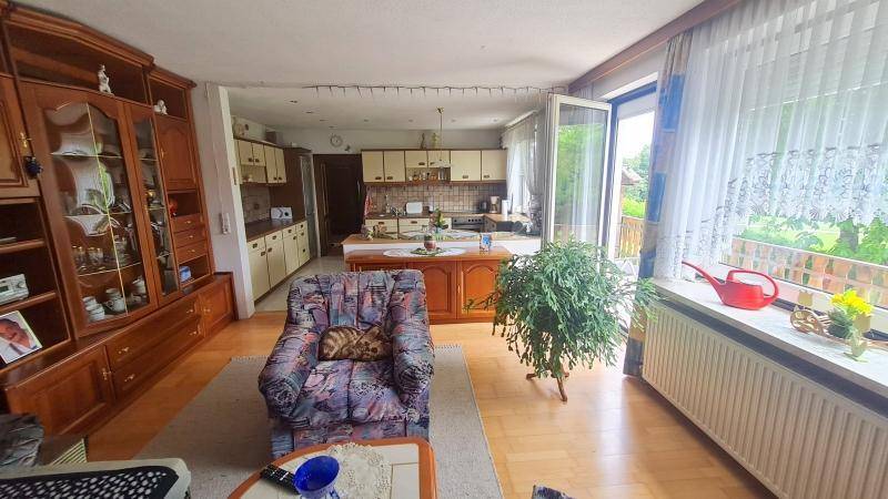 Helles Wohnzimmer mit Holzmöbeln, Parkettboden und offenem Übergang zur Küche sowie Balkonzugang.