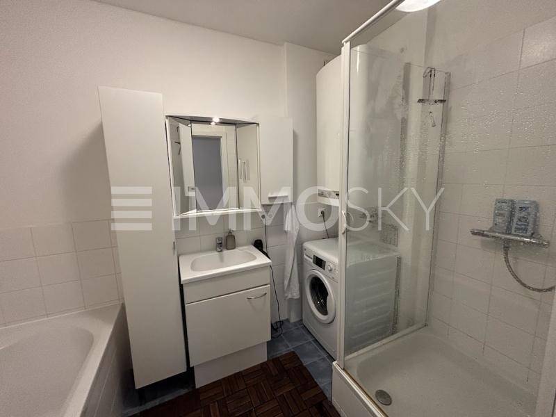 Funktionales Badezimmer mit Badewanne, Duschkabine, Waschbecken und integrierter Waschmaschine.