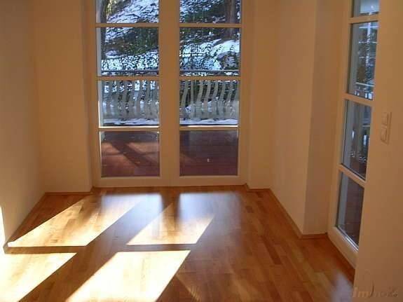 Heller Raum mit Holzboden und großen Fenstertüren, die auf einen schneebedeckten Balkon führen.