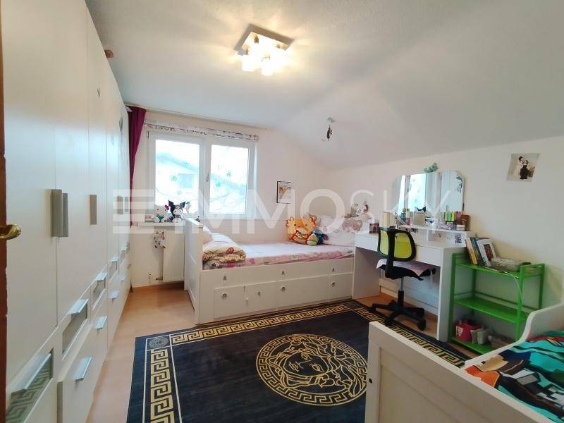 Kinderzimmer mit zwei Betten, Schreibtisch und weißen Kleiderschränken unter Dachschräge.
