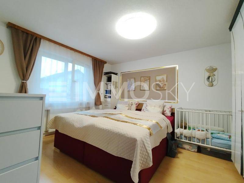 Gemütliches Schlafzimmer mit großem Bett, weißer Kommode und Babybett am Fenster.