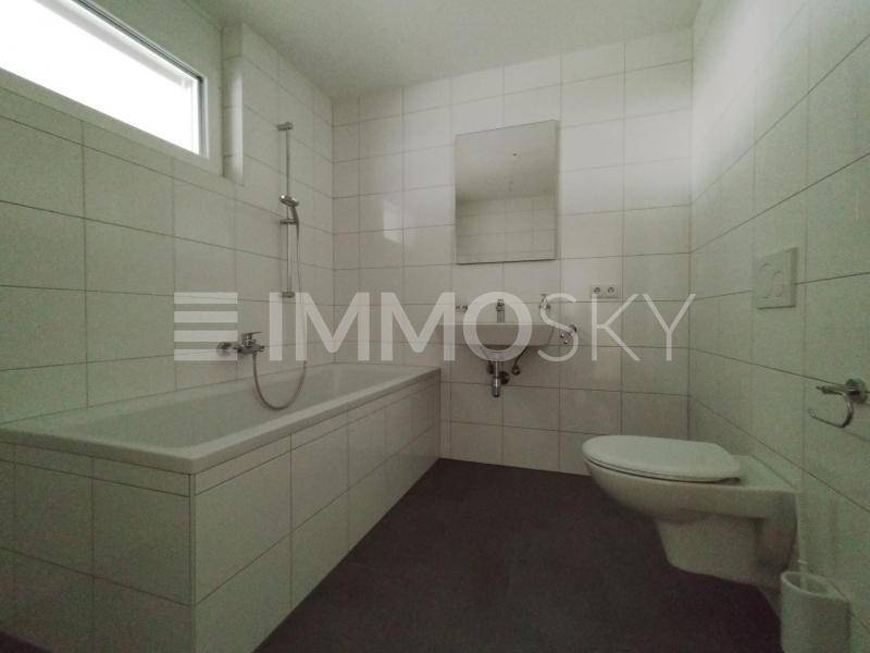 Modernes Badezimmer mit weißen Fliesen, Badewanne, wandhängendem WC und Fenster für Tageslicht.
