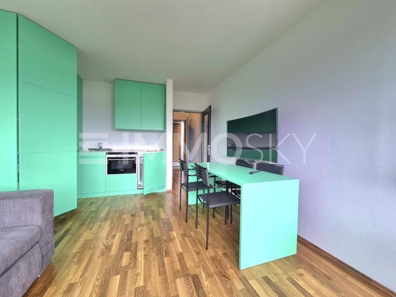 Offener Wohnbereich mit integrierter grüner Küchenzeile, Esstisch und Sofa auf Holzboden.