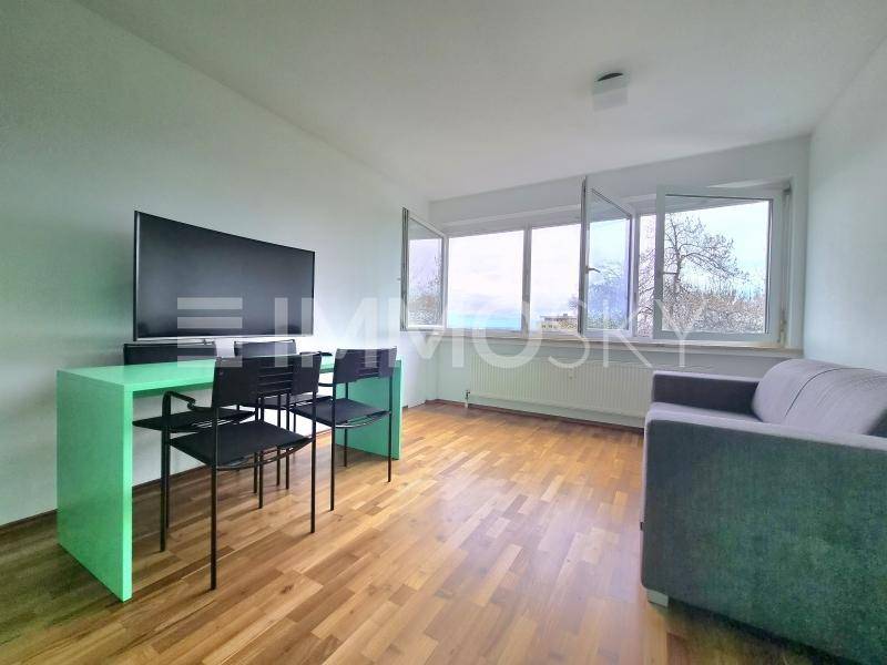 Heller Wohnbereich mit Sofa, modernem Esstisch und großem Fernseher, mit Blick ins Grüne.