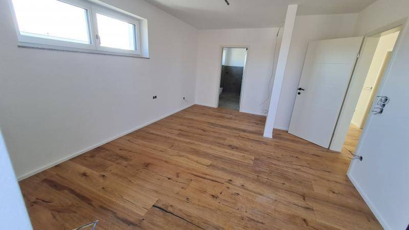Helles Schlafzimmer mit Holzplankenboden und Fenster, angrenzend an ein Badezimmer.