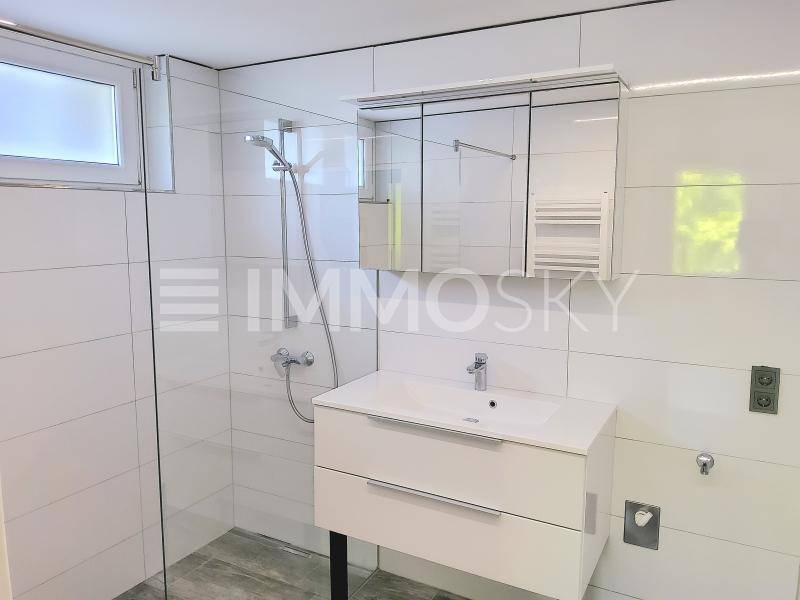 Modernes Badezimmer mit weißen Fliesen, einer Dusche und einem Waschtisch mit Spiegelschrank.