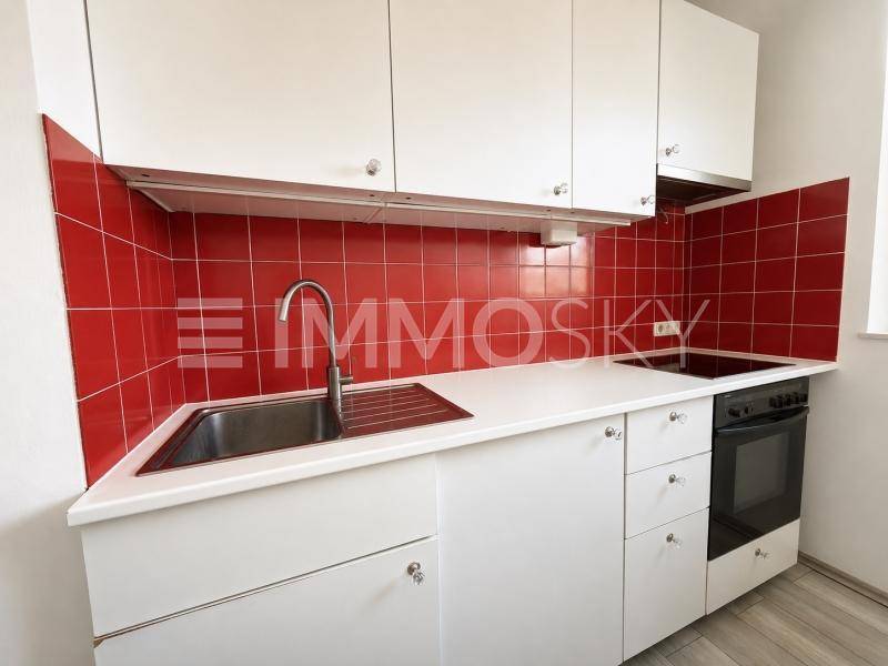 Funktionale Küchenzeile mit weißen Schränken, rotem Fliesenspiegel und integriertem Herd mit Backofen.