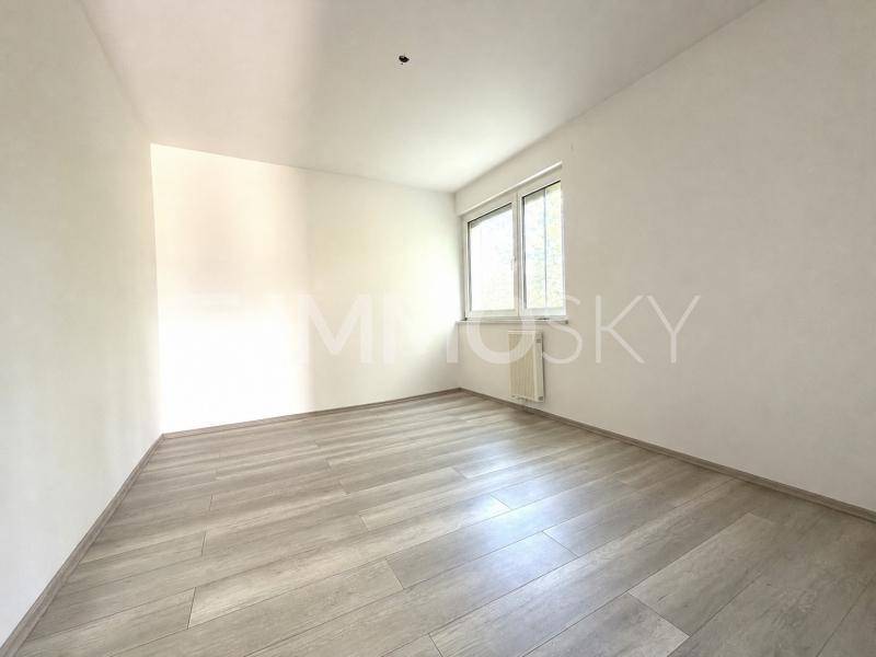 Helles Schlafzimmer mit hellem Laminatboden und einem Fenster, das viel natürliches Licht hereinlässt.