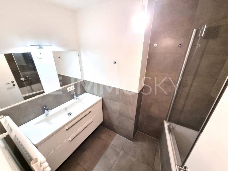 Modernes Badezimmer mit doppelter Waschtischplatte, grauen Fliesen und Duschbereich.