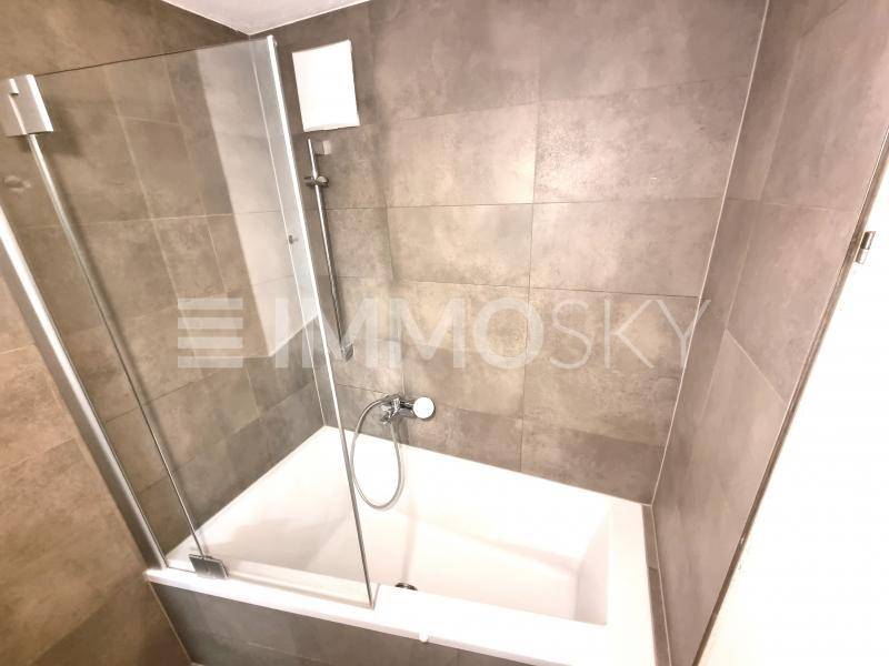 Badezimmer mit Badewanne, Duschabtrennung und grauen Wand- und Bodenfliesen.