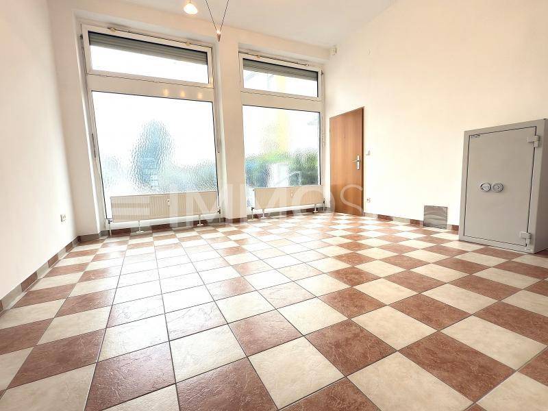 Großer Ladenraum mit hellen Wänden, Fliesenboden, großen Fenstern und einem Sicherheitssafe.
