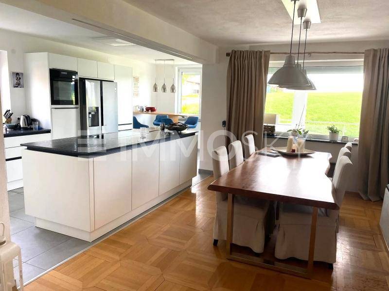 Offene Küche mit weißer Insel und Essbereich mit großem Holztisch und Parkettboden.