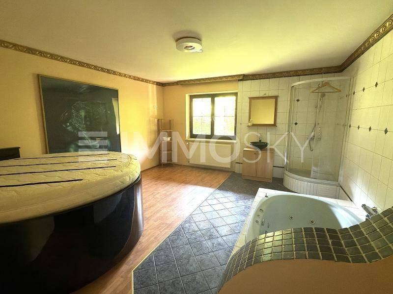 Geräumiges Schlafzimmer mit rundem Bett, Eckdusche und Whirlpool-Badewanne, teilweise gefliest.