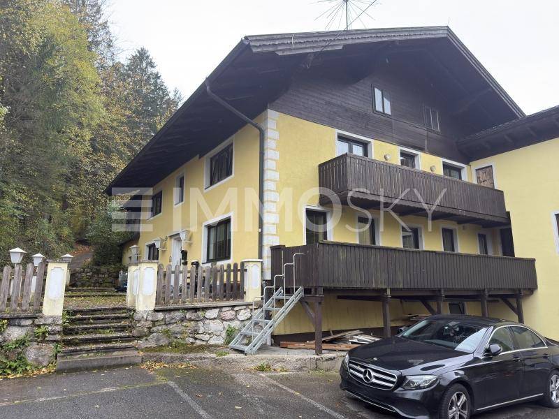 Gelbes Wohnhaus mit mehreren Balkonen und einem geparkten Auto vor dem Eingangsbereich.