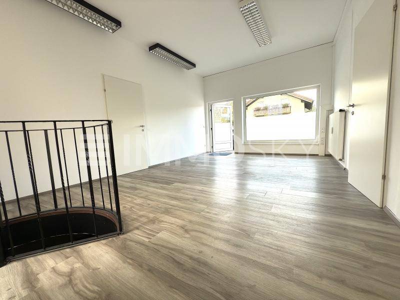 Heller, leerer Raum mit Laminatboden, großen Fenstern und einer Wendeltreppe.