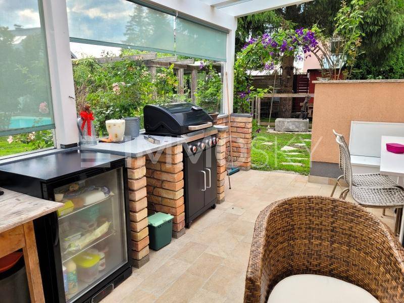 Überdachte Außenküche mit Grill, Kühlschrank und gemütlichem Sitzbereich im Wintergarten.