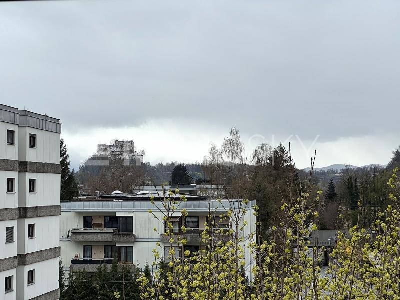 Blick aus dem Fenster auf umliegende Gebäude, Bäume und eine entfernte Burg auf einem Hügel.
