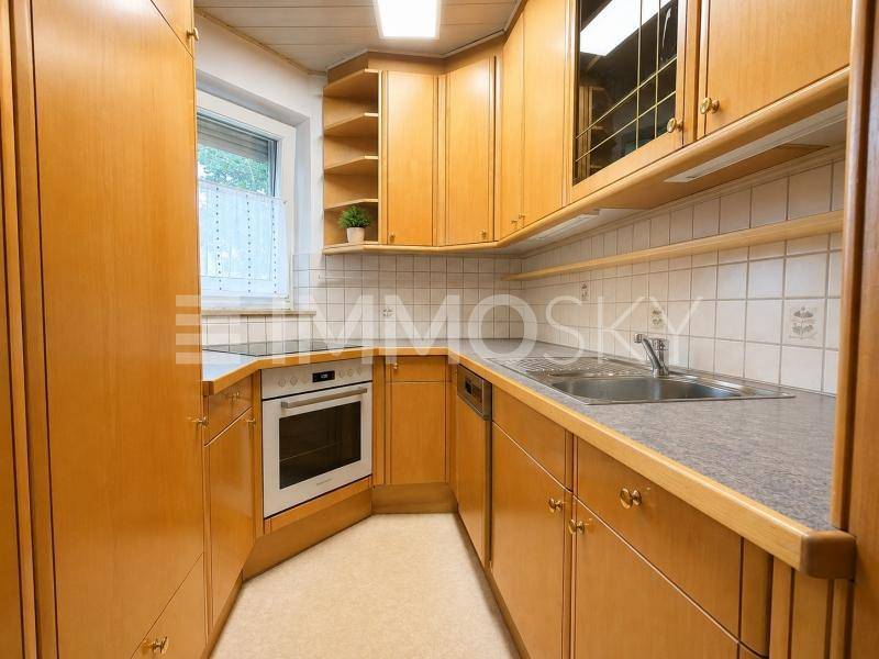 Funktionale Küche mit Holzschränken, Fliesenboden und integrierten Geräten.