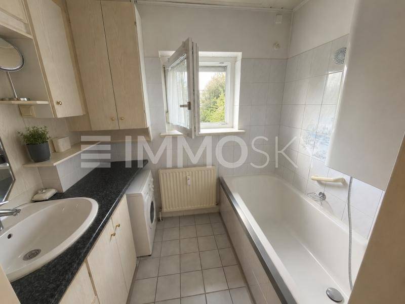 Helles Badezimmer mit Badewanne, Waschbecken, Waschmaschine und Fenster.