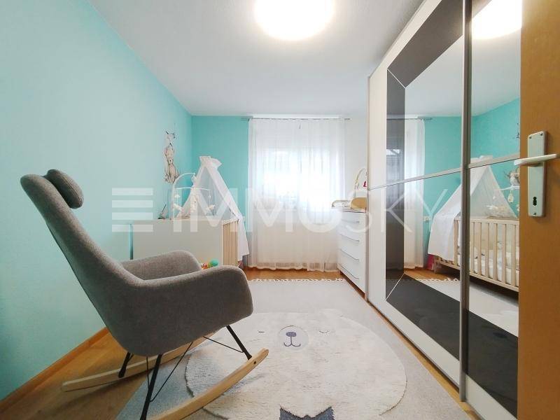 Kinderzimmer mit Schaukelstuhl, Babybett und Spiegelschrank in hellblauer Wandfarbe.