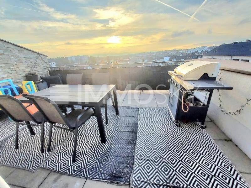 Geräumige Dachterrasse mit Esstisch, Grillbereich und weitem Blick über die Stadt bei Sonnenuntergang.