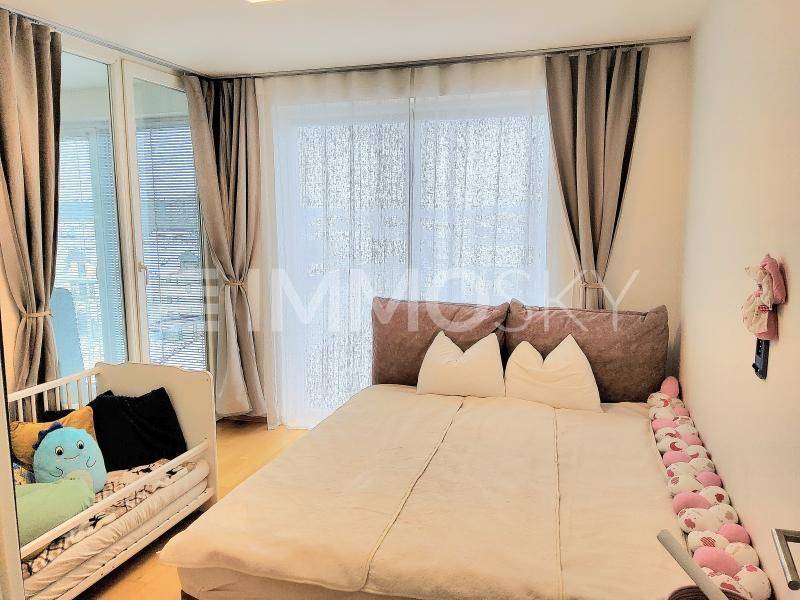 Gemütliches Schlafzimmer mit Doppelbett, Babybett und großen Fenstern mit Vorhängen.
