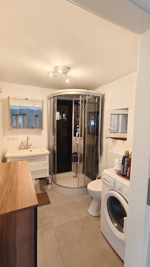 Modernes Badezimmer mit Duschkabine, Waschbecken, Toilette und integrierter Waschmaschine.