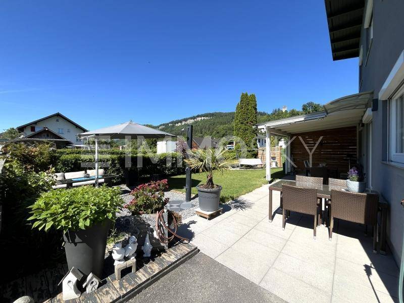 Sonniger Terrassenbereich mit Gartenmöbeln, Rasenfläche und weitem Blick auf die Hügellandschaft.