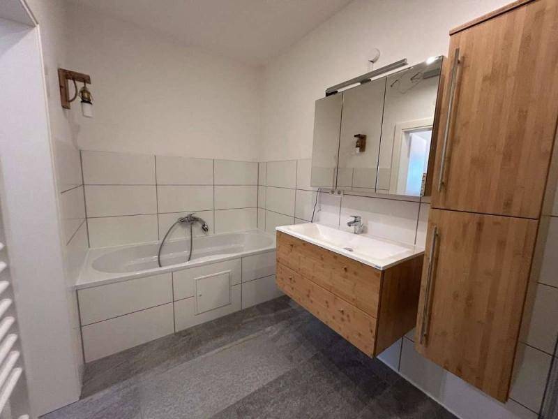 Modernes Badezimmer mit Badewanne, einem einzelnen Waschbecken und Holzschränken.
