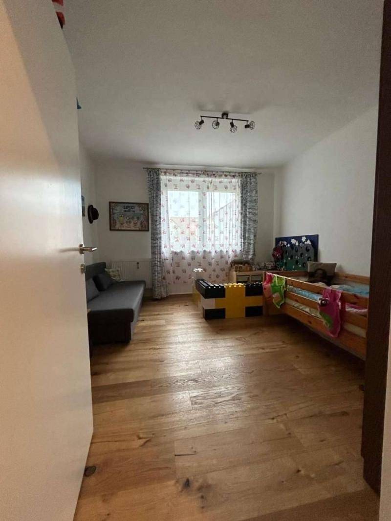 Helles Kinderzimmer mit Holzboden, einem Kinderbett und einem kleinen Sofa.