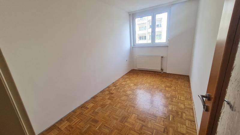 Weiteres leeres Zimmer mit Parkettboden und einem großen Fenster für natürliche Beleuchtung.