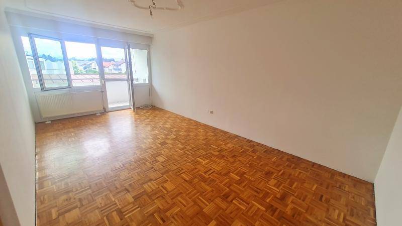 Helles, leeres Wohnzimmer mit Fischgrätparkettboden und Zugang zu einem Balkon.